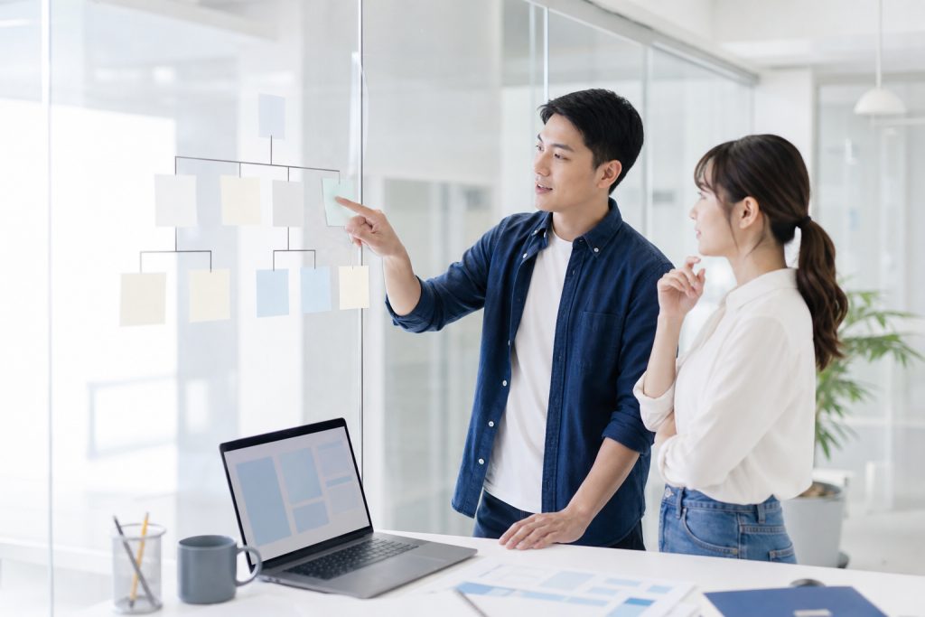 AI 示意圖：網站顧問與企業主在玻璃牆前用便利貼排出網站架構，討論網站架設步驟